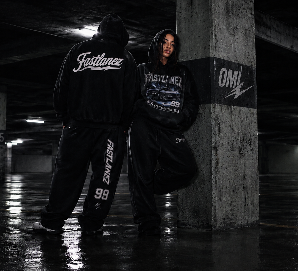 FASTLANEZ Drop 01 campaign — two models in black graphic hoodies and matching pants in a dark concrete parking garage